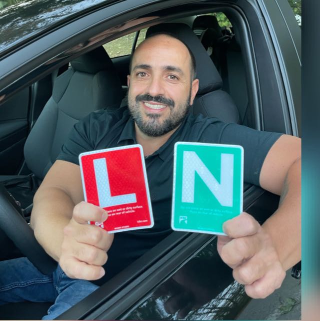 Fabio, the Marques Driving School instructor, holding ICBC L and N signs from the driver’s seat